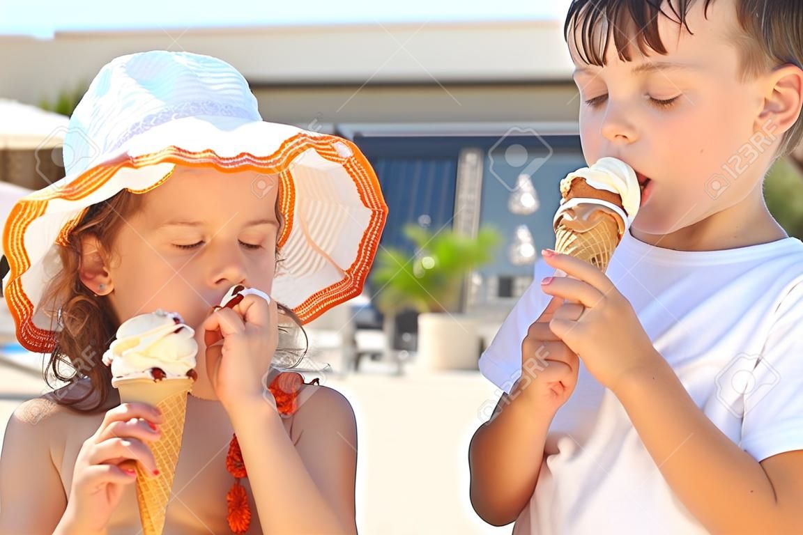 El hermano y la hermana pequeña comiendo un helado después de bañarse. Niña llevaba traje de baño y sombrero