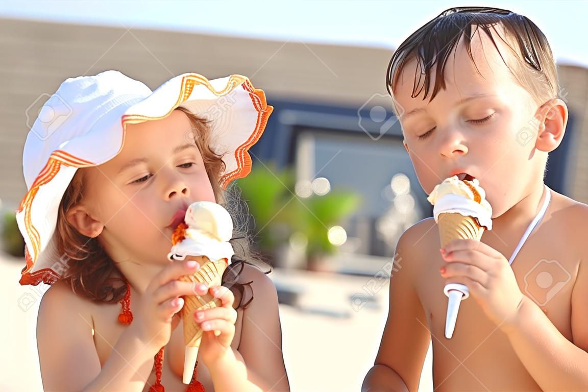 El hermano y la hermana pequeña comiendo un helado después de bañarse. Niña llevaba traje de baño y sombrero