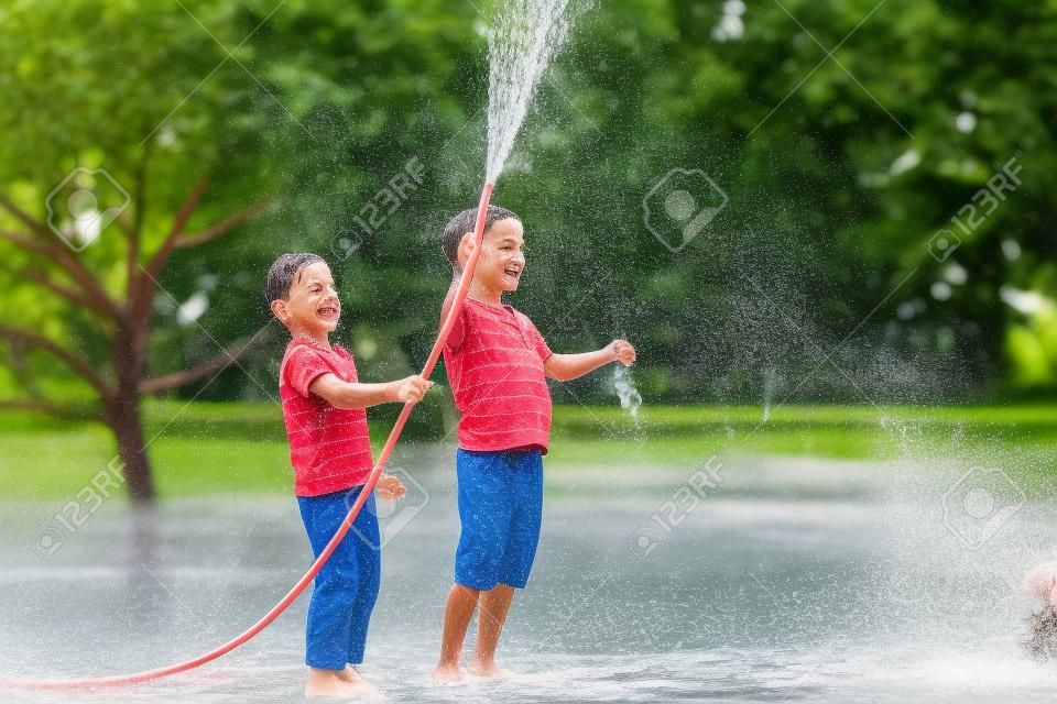 Brothers having fun splash each other with water in the village. Boys having fun with watering fruit garden in village outdoors. Funny holiday leisure water for children.
