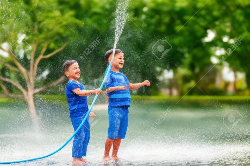 Brothers having fun splash each other with water in the village. Boys having fun with watering fruit garden in village outdoors. Funny holiday leisure water for children.