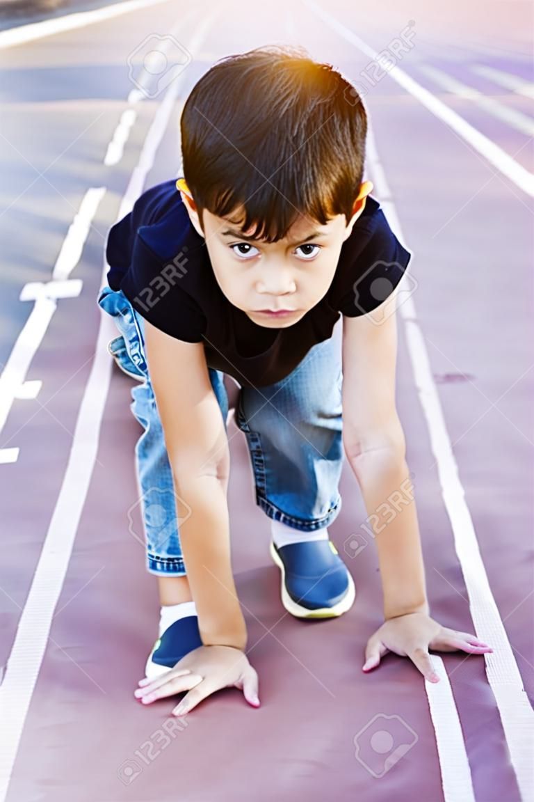 Menino de escola saudável pronto para correr no ponto de partida, conceito de competição ativa