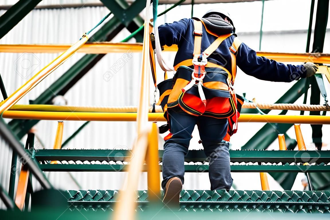 Bouwarbeider die veiligheidstuig en veiligheidslijn draagt die op een hoge plaats werkt
