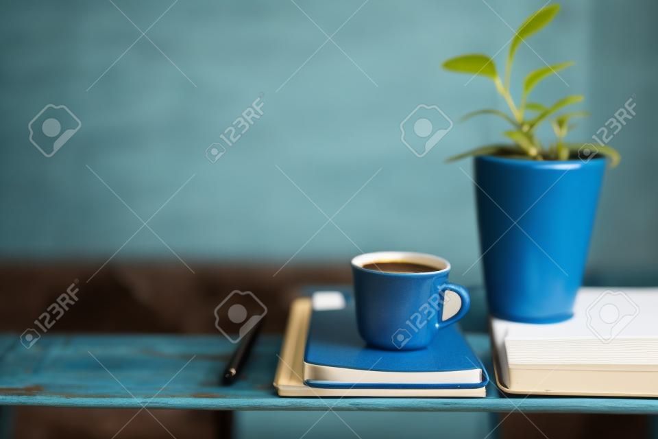 Koffiemok en notebook en Baby Rubber Plant op verweerde blauwe houten tafel