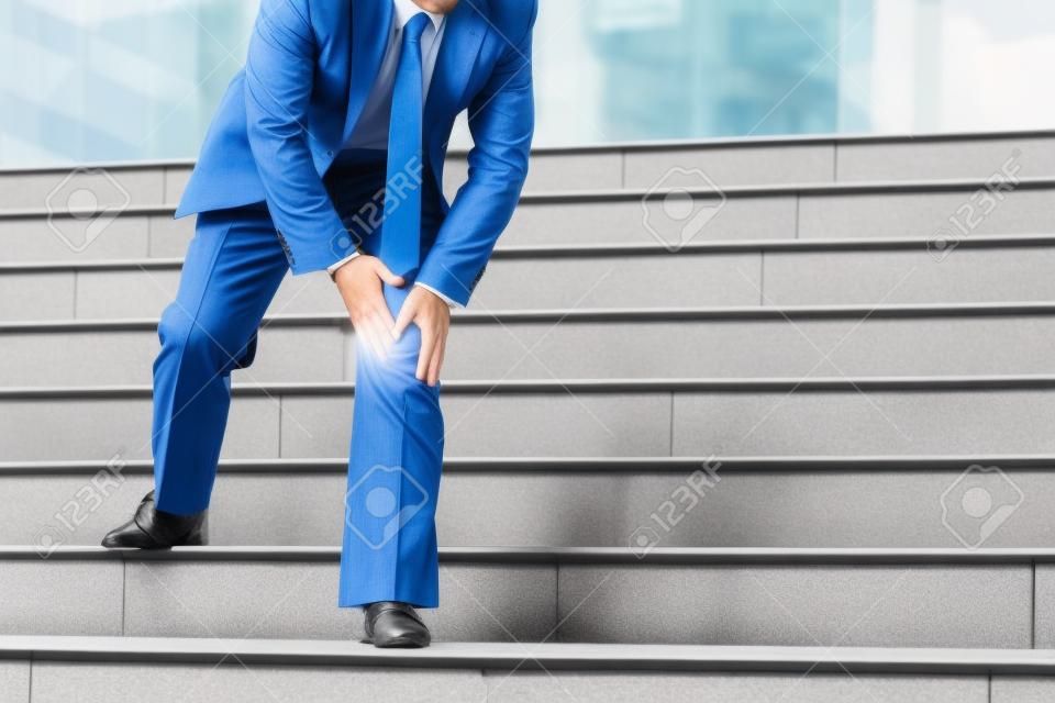 Businessman have the pain and painful knee expression and sit down on the stairs during go to office