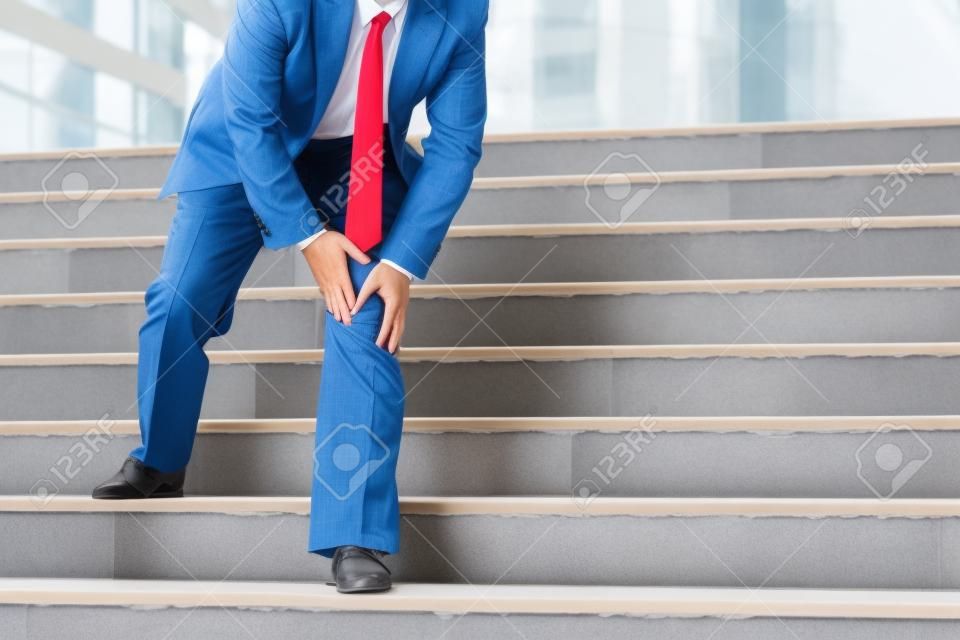 Businessman have the pain and painful knee expression and sit down on the stairs during go to office