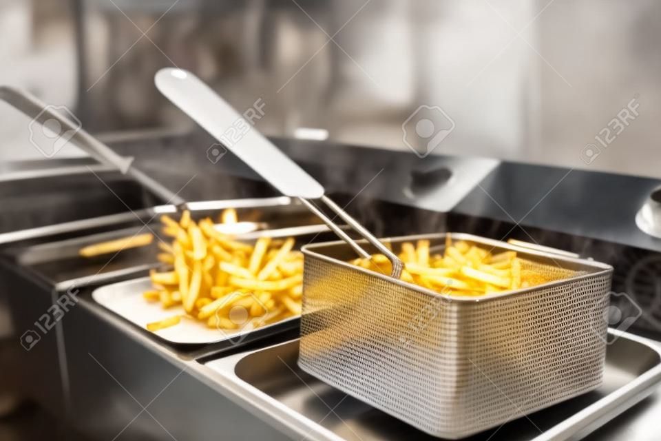 French fries cooking. Grid with strips hop potato lowered into boiling oil. Concept of fast food, delicious food, restaurant