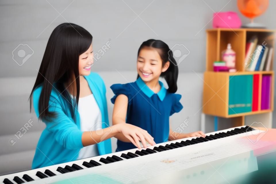 Schöner asiatischer Pianistenlehrer, der einem Mädchen beibringt, Klavier zu spielen, Musikausbildungskonzept.