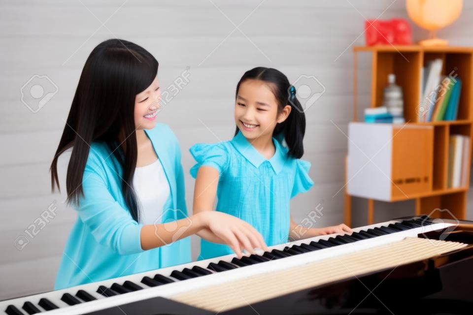 Hermosa profesora de pianista asiática enseñando a una niña a tocar el piano, concepto de educación musical.
