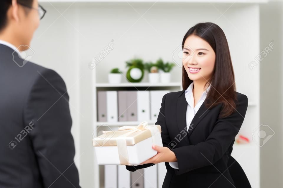 Bella giovane donna di affari asiatica che dà il regalo di natale al suo capo in ufficio