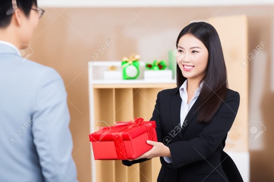 Bella giovane donna di affari asiatica che dà il regalo di natale al suo capo in ufficio