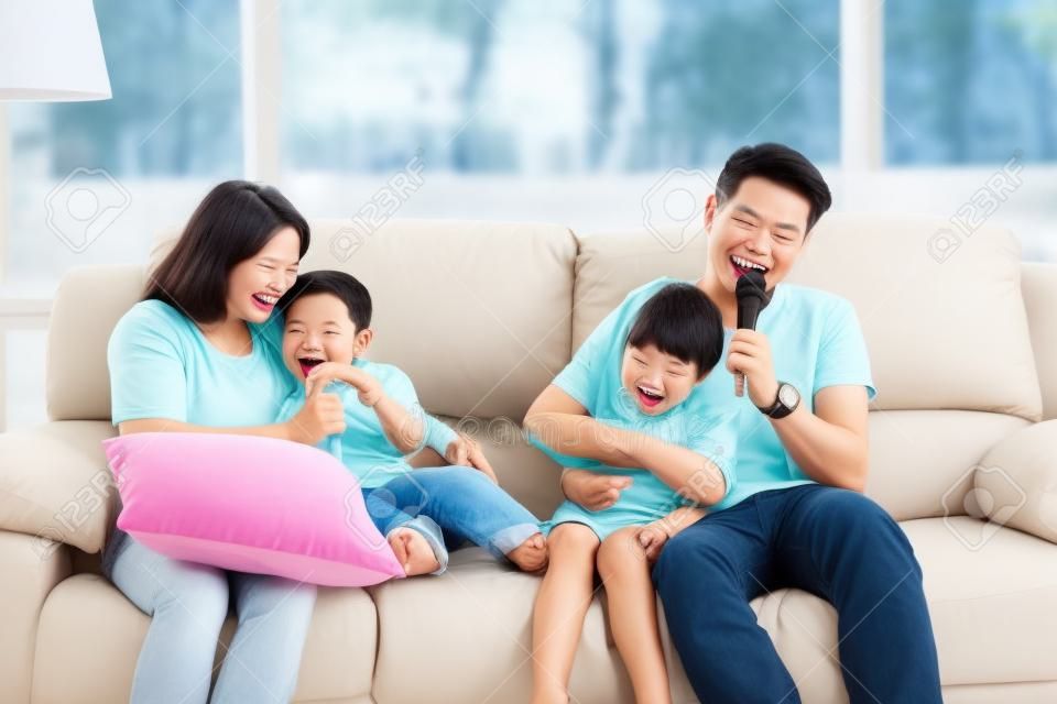 Glückliche asiatische Familie, Vater, Mutter, Tochter und Sohn, die Karaoke auf dem Sofa im Wohnzimmer mit glücklichem Lächeln singen (Entspannungs- und Technologiekonzept)