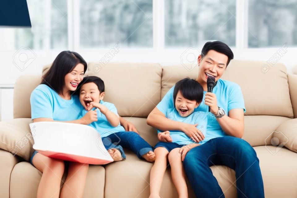 Família asiática feliz, pai, filha mãe e filho cantando karaokê no sofá na sala de estar com rosto sorridente feliz (relaxamento e conceito de tecnologia)