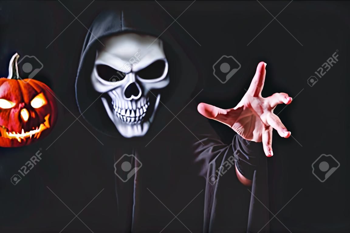 Fato de demônio de terror com crânio de abóbora assustador em preto vestido para o carnaval de Halloween. Cosplay de diabo segurando máscara fantasma e levantar a mão com espaço de cópia em branco para o seu conteúdo de publicidade.
