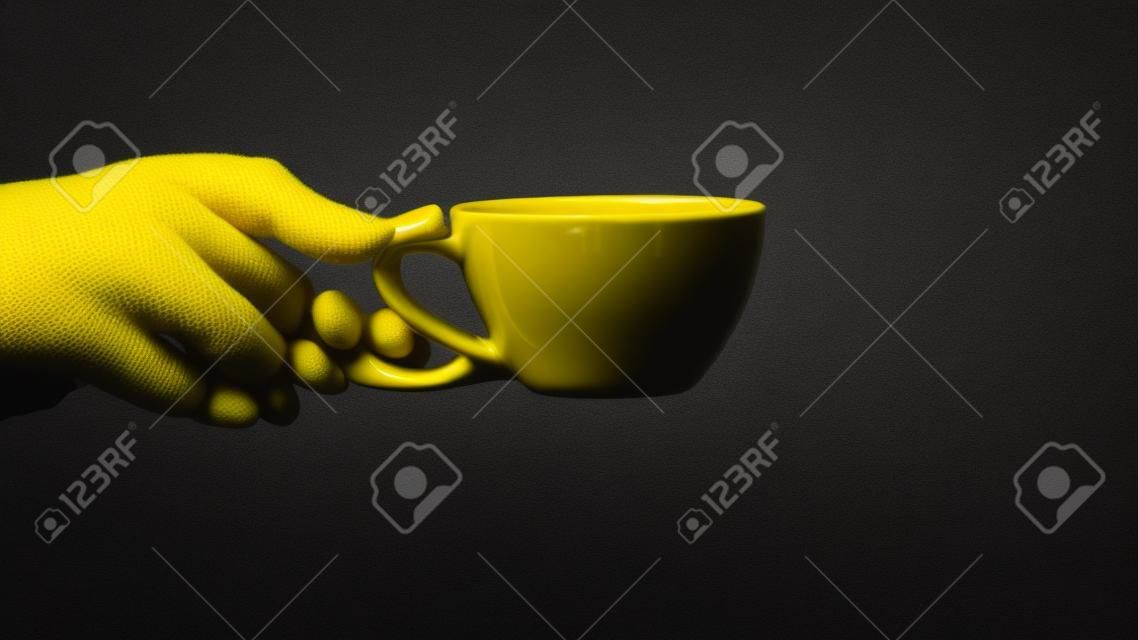 Close-up isolated hand holding yellow mug on black background. Hand hold simple yellow cup. Perfect for both tea and coffee.