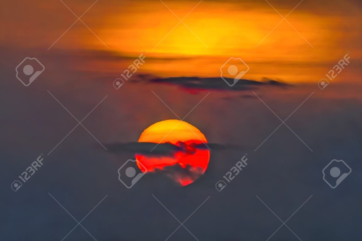 Beautiful sunset. Dramatic Fiery Sun Surrounded by Clouds During Sunset.  Vibrant orange red clouds are back lit by the sun.