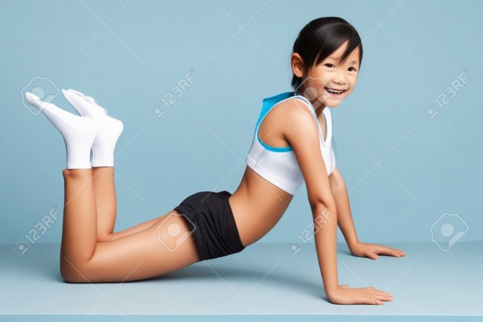 Piccola ragazza asiatica facendo esercizi di fitness, isolati su bianco