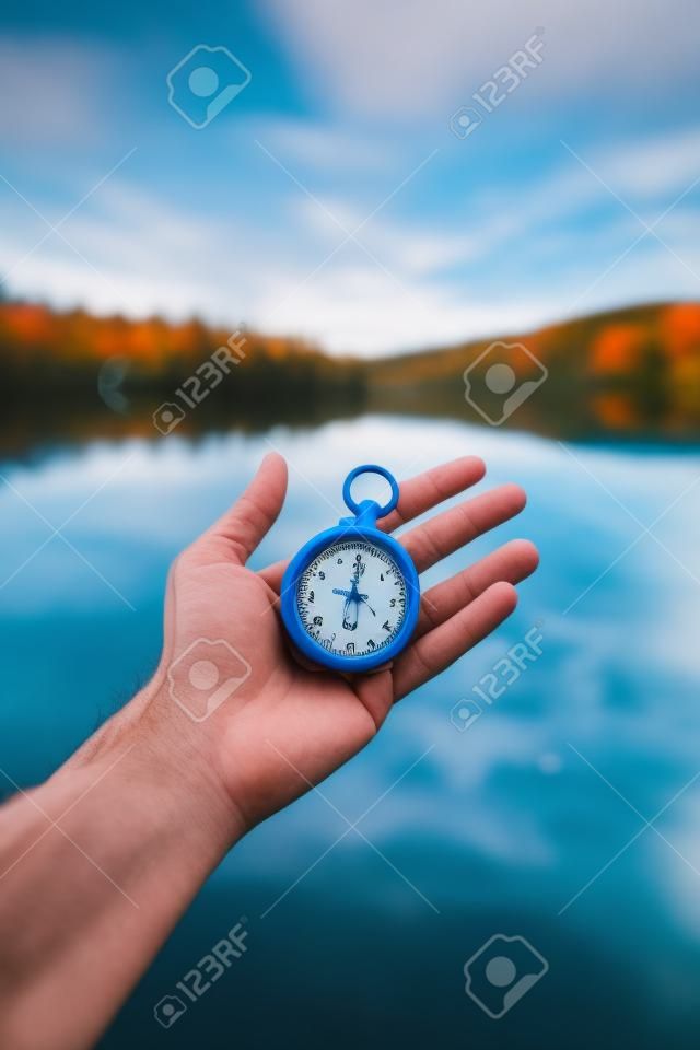 Hand held stop watch outdoors, autumn, blurry blue lake in the background