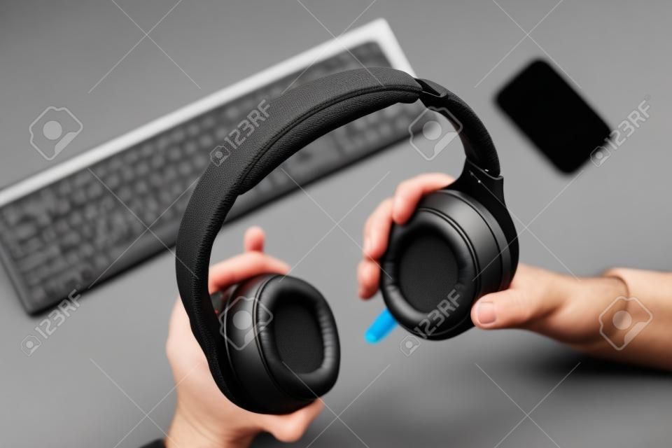 Male hands are holding black wireless headphones, workspace