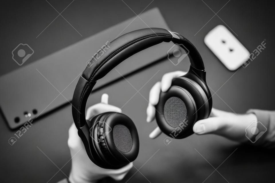 Male hands are holding black wireless headphones, workspace