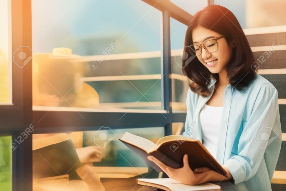 窓の近くで本を読んでコーヒーを持っている魅力的なアジアの学生(女性)の肖像画。ライフスタイルは、概念を準備教育試験をリラックスします。ヴィンテージ朝光