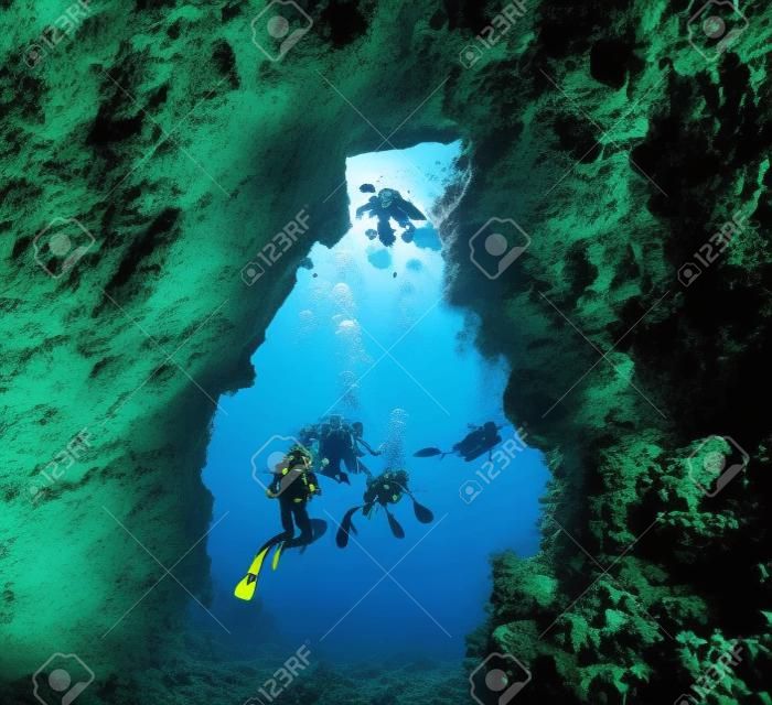 Los buzos que exploran una cueva submarina de un arrecife de coral tropical