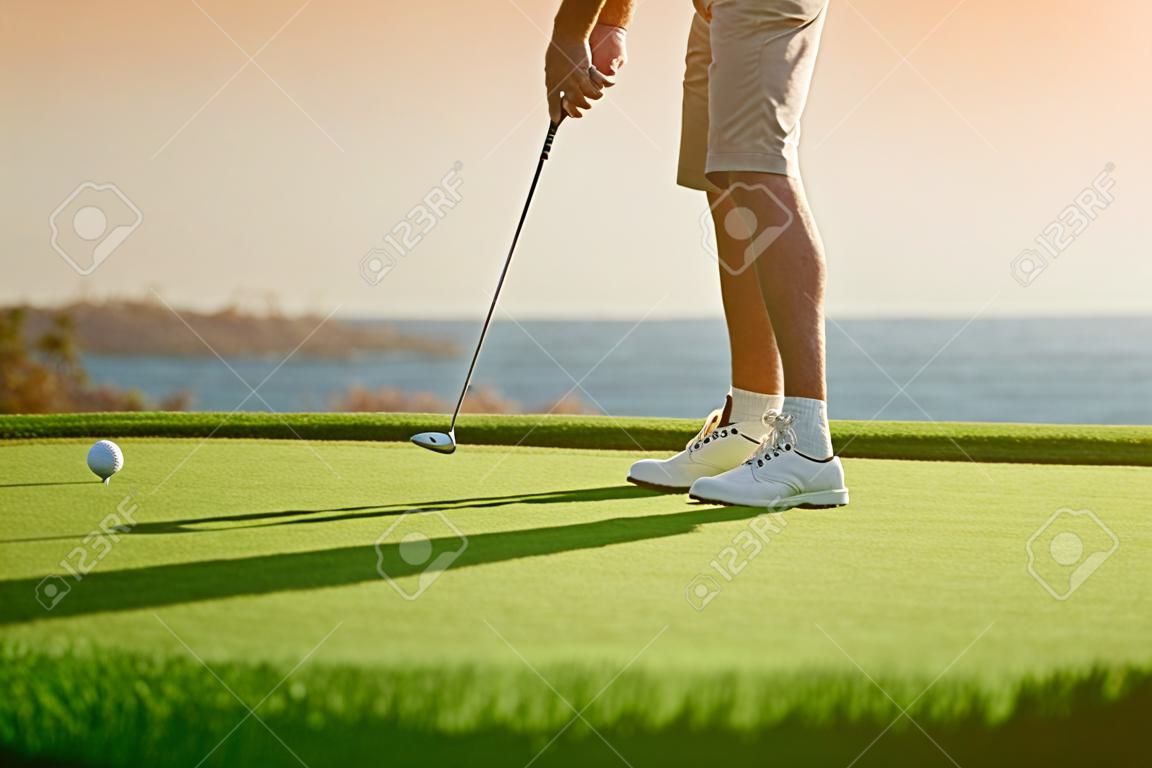 Golfjátékos fog tee off napnyugtakor, óceán, horizont