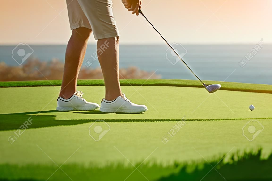 Golfjátékos fog tee off napnyugtakor, óceán, horizont