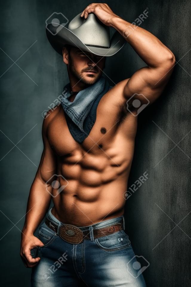 Photo de bel homme musclé posant dans un chapeau de cowboy et des jeans sur le mur grunge.