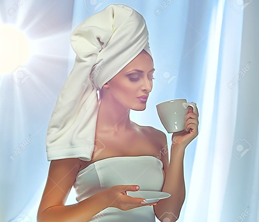 Красивая привлекательная женщина пить кофе. Девушка с белым полотенцем на голове. Утро фото.
