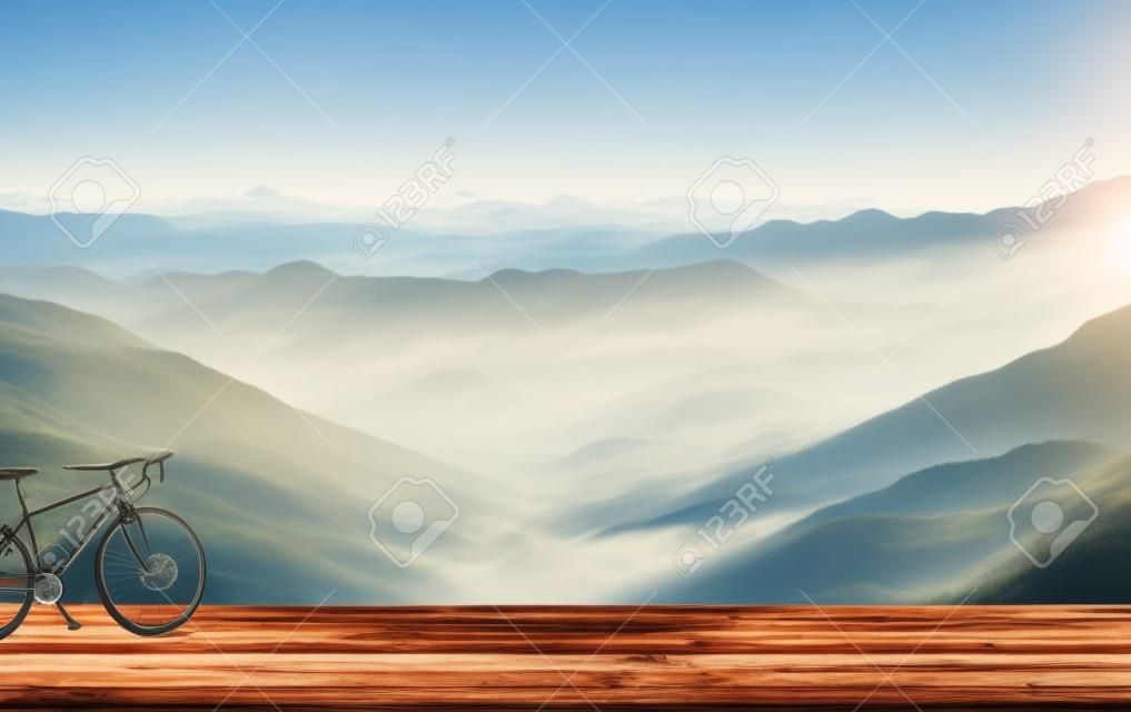 Bicycle on wooden table with misty mountains in the background.