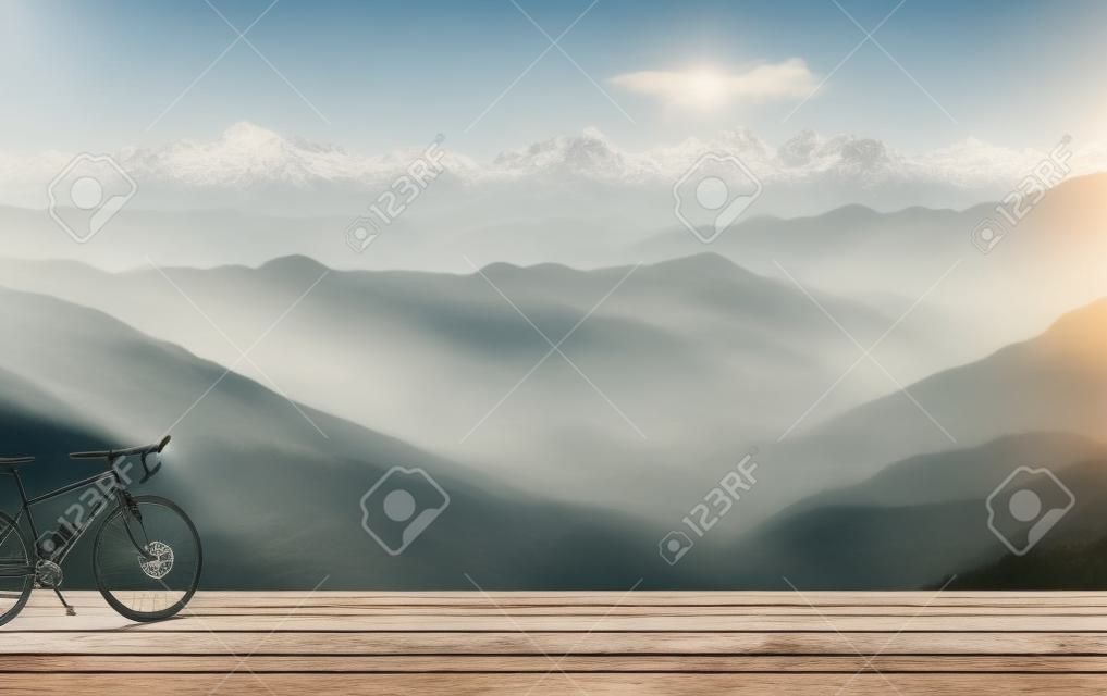 Bicycle on wooden table with misty mountains in the background.