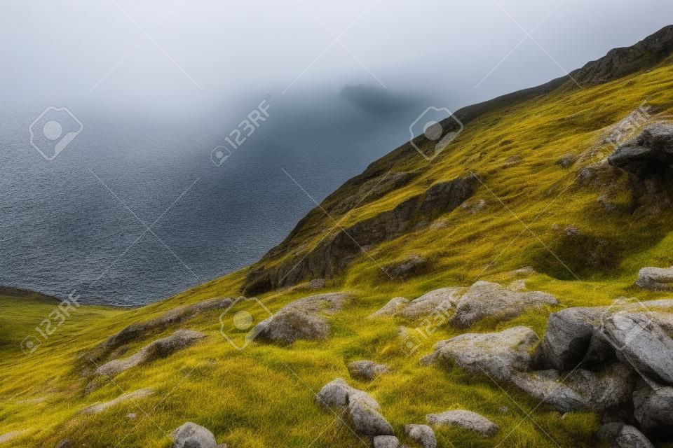 edge of steep slope on rocky hillside in foggy weather. dramatic scenery in mountains