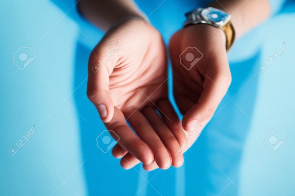 Eu estou diante de você com as mãos bem abertas. closeup de uma pessoa irreconhecível que se estende com as mãos abertas contra um fundo azul.