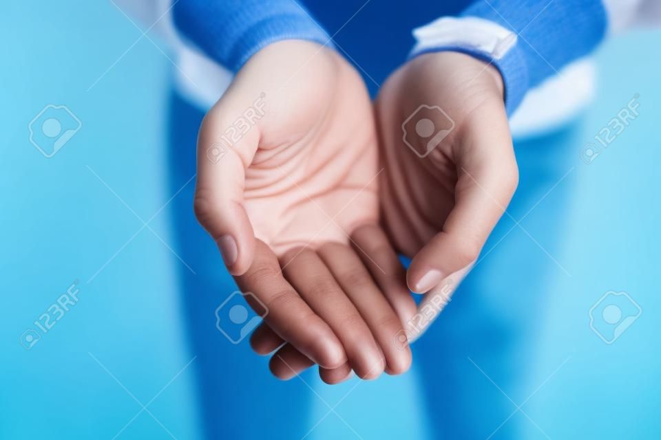 I stand before you with hands wide open. Closeup of an unrecognizable person reaching out with their open hands against a blue background.