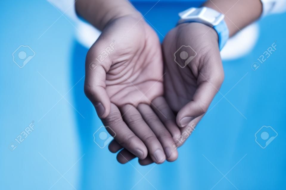 I stand before you with hands wide open. Closeup of an unrecognizable person reaching out with their open hands against a blue background.