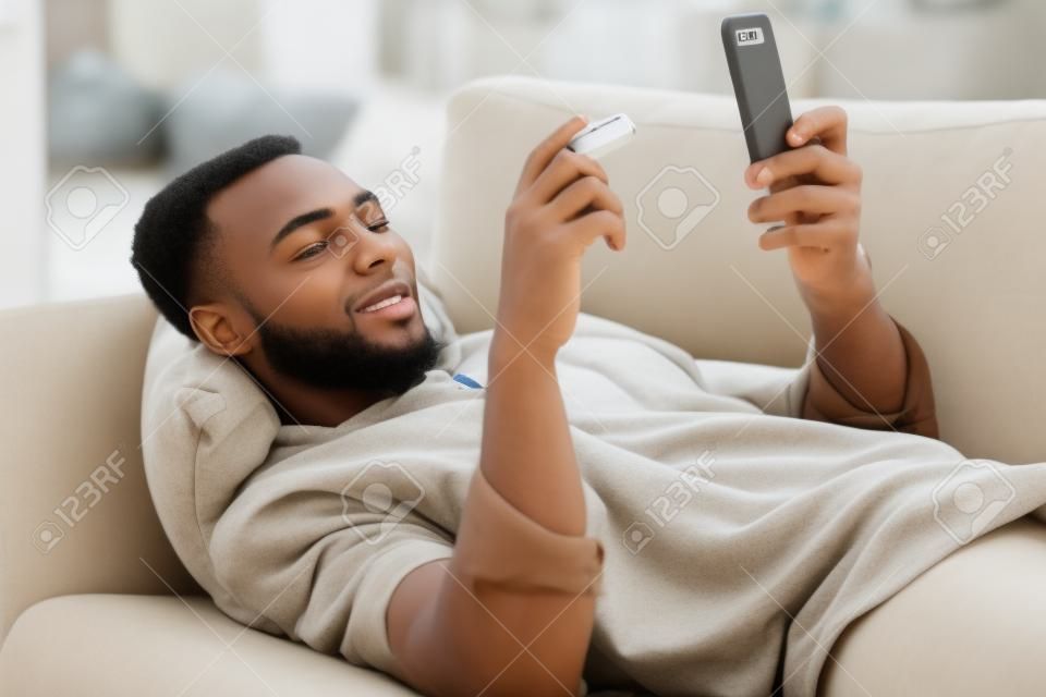 Comprando desde la comodidad de mi sofá. Una foto de un joven que usa una tarjeta de crédito y un teléfono en el sofá de su casa.