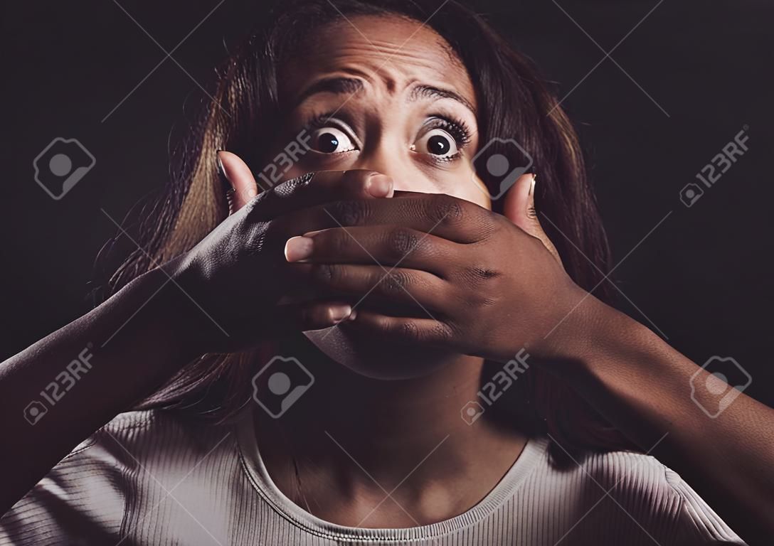 You wake up every morning to fight the same demons. Shot of a scared young womans mouth being covered by an unrecognisable mans hand against a black background.