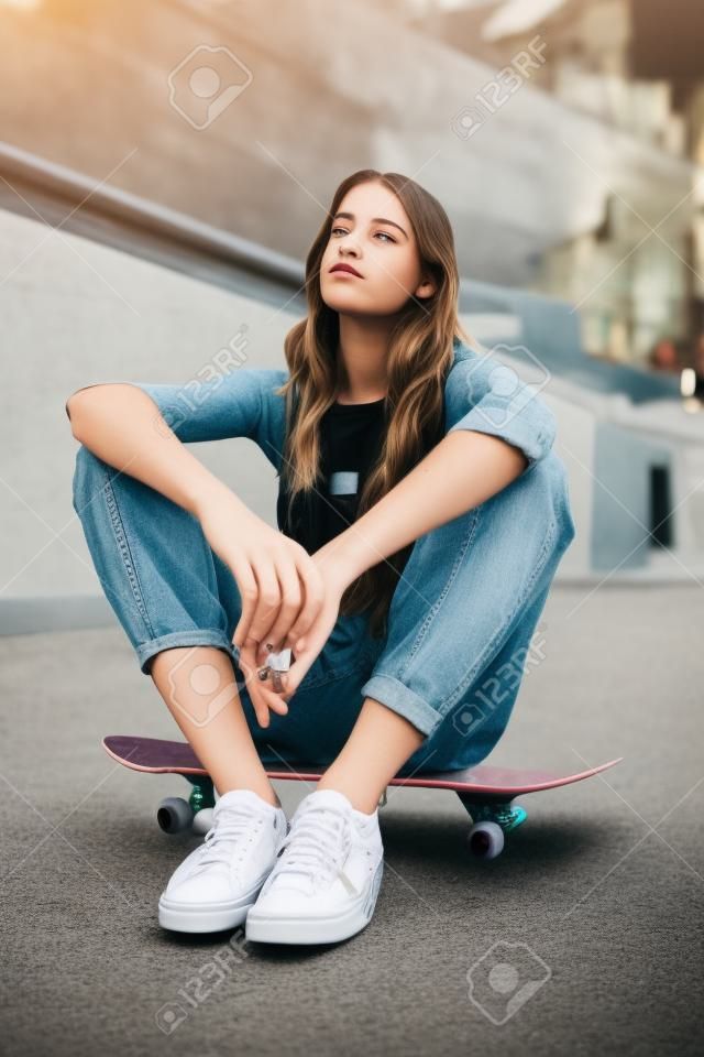 Menina de skate hipster, relaxe na rua da cidade e pensando em um futuro parque de skate de skate legal. Jovem mulher urbana, moda casual criativa e elegante gen z adolescente sentado no sol da Califórnia