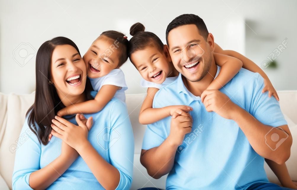 Happy family, mother and father with children in a portrait in a sofa bonding hugging and laughing together. Mom, dad and fun Mexican kids playing, kissing parents and enjoying quality time in Mexico