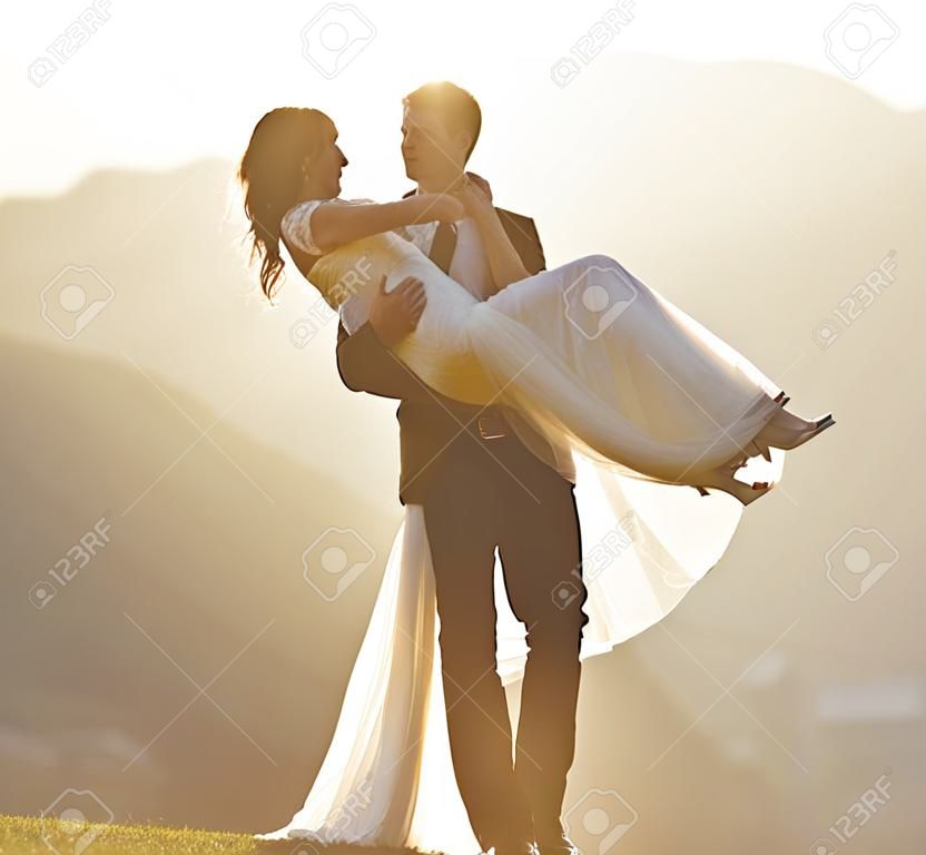 Er trägt seine Braut in den Sonnenuntergang. ein Bräutigam, der seine Braut trägt.
