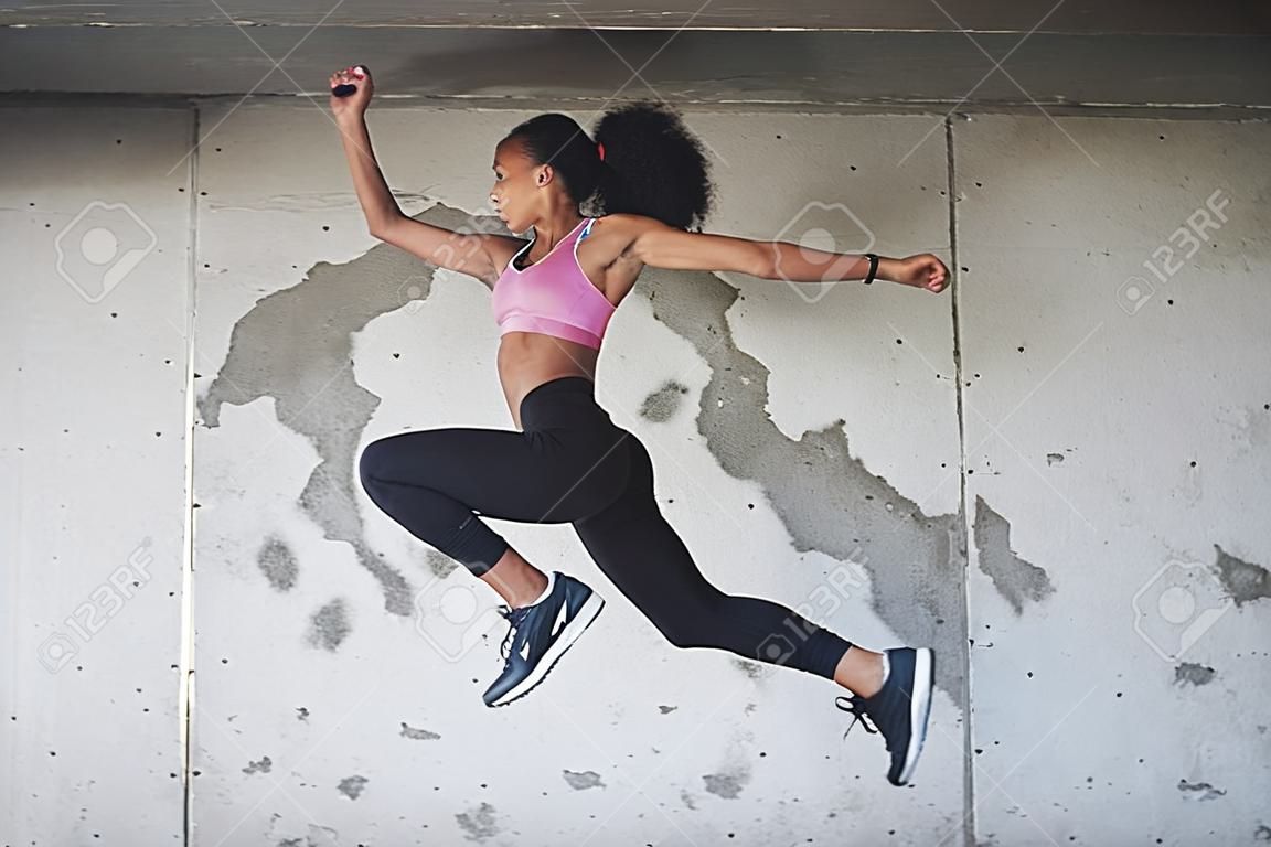Reaching new heights everyday. Full length shot of an athletic young sportswoman jumping in the air against a wall outdoors.