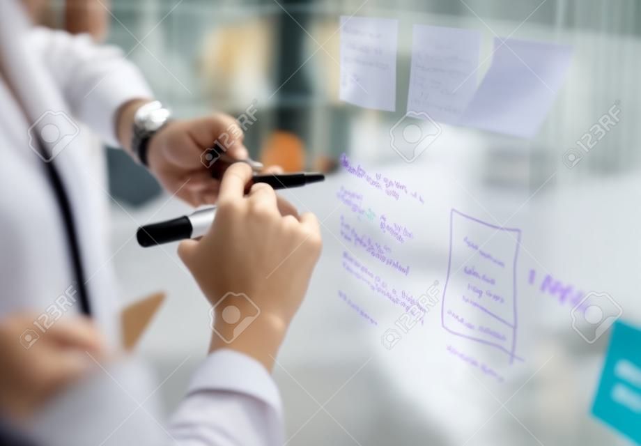 Marking their ideas as they go. Closeup shot of two businesswomen brainstorming with notes on a glass wall in an office.