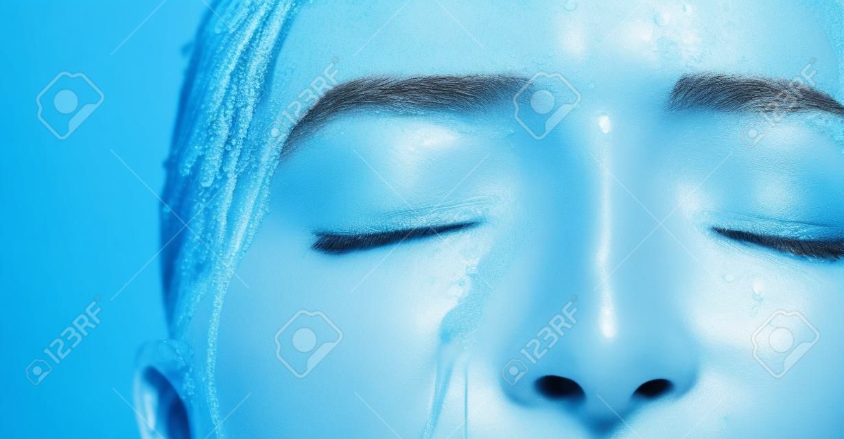 Shower water, face cleaning and black woman washing with liquid for hydration, beauty healthcare or skincare hygiene. Self care studio, spa salon and relax closeup model isolated on blue background