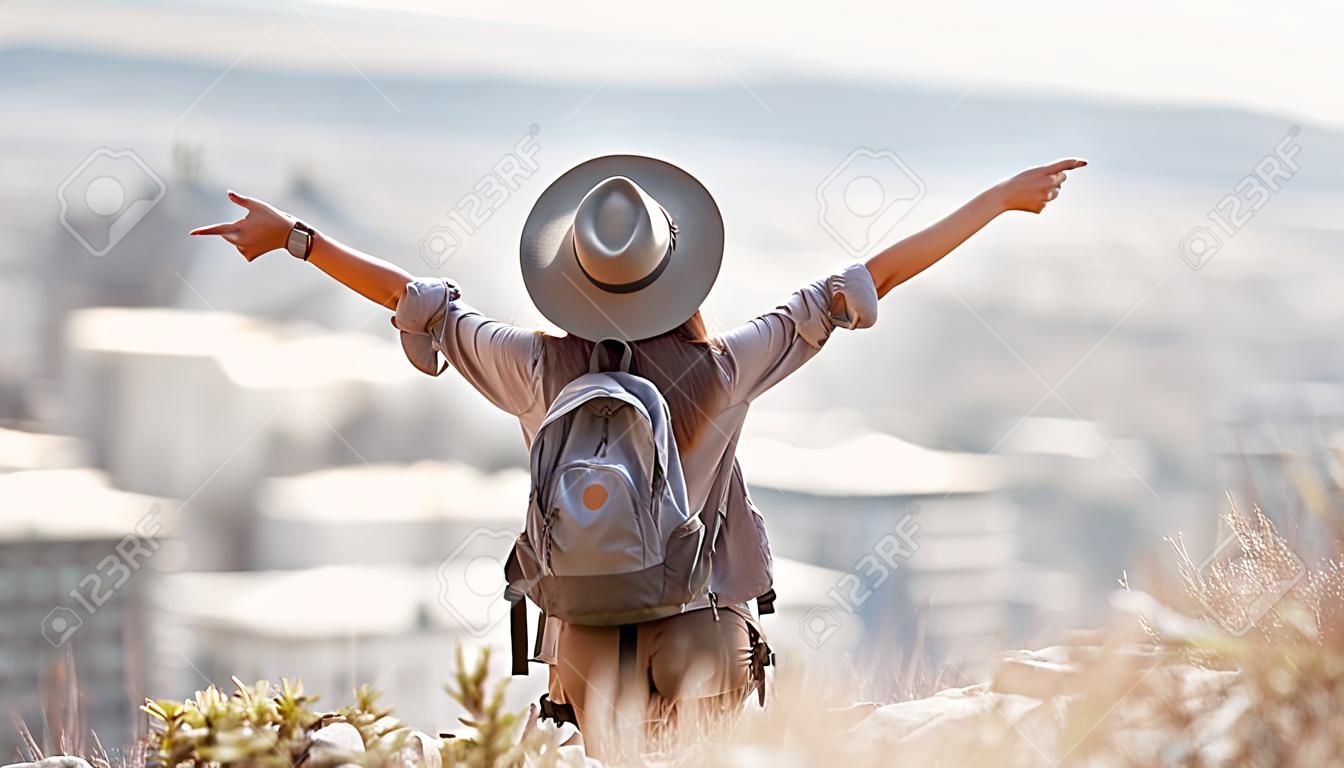 Woman, tourist and hiking or travel freedom in city for adventure, backpacking or journey on mountain in nature. Female hiker with open arms enjoying fresh air, trekking or scenery of an urban town