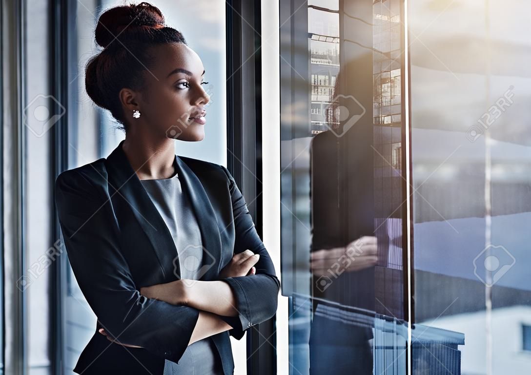 Business woman, window and thinking for vision, goals and future of career with ideas, mission and mindset. Young businesswoman, focus and ambition in workplace with memory, reflection and dream