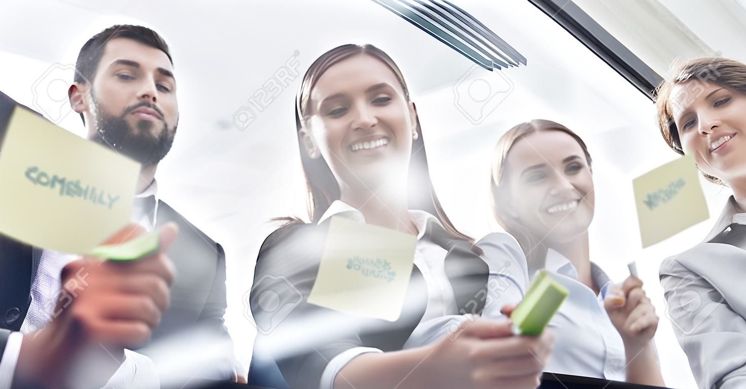 Planning, writing and business people on glass board for teamwork, brainstorming and schedule or workflow notes. Happy women, manager and group or team with sticky note ideas, solution and window