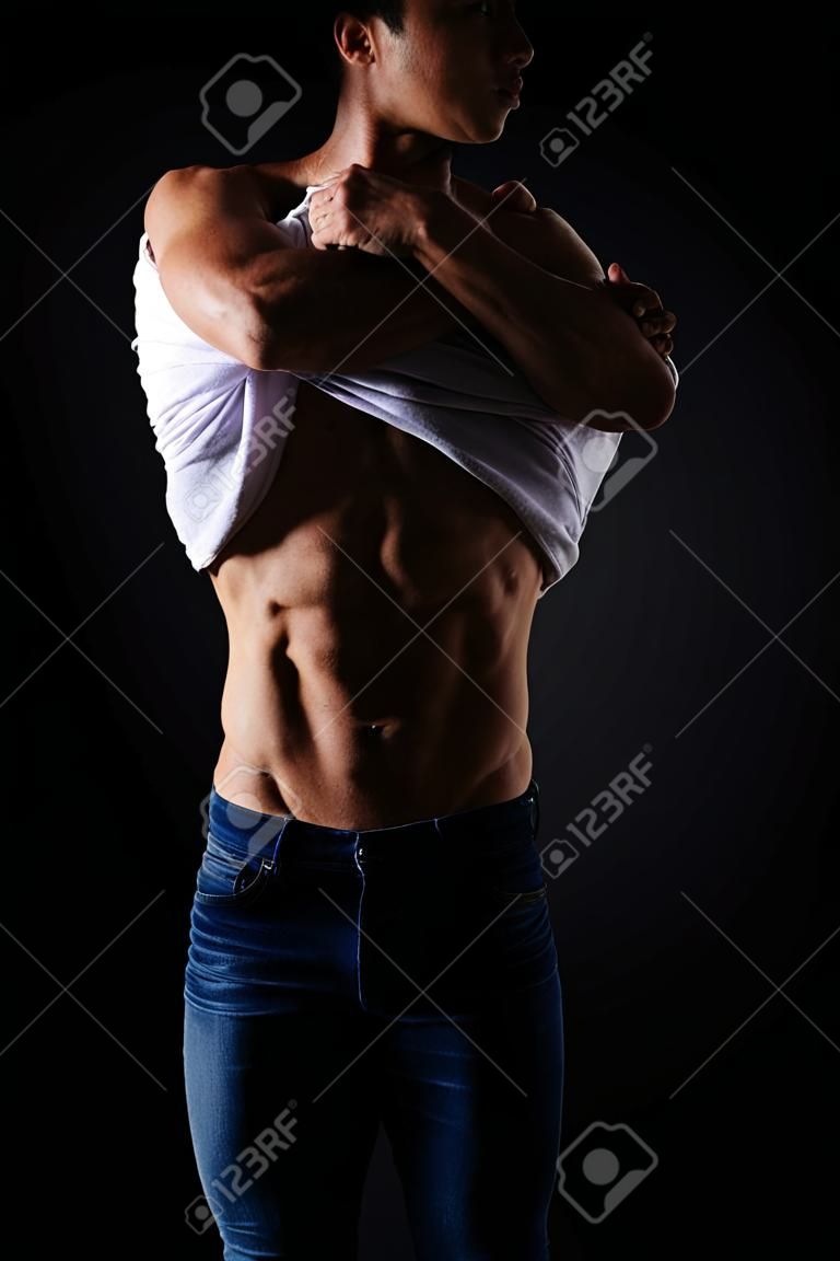 Il corpo muscoloso e l'uomo si tolgono la maglietta per mostrare la pelle e lo stomaco per l'allenamento benessere e l'allenamento in studio bodybuilder e l'uomo rimuove la maglietta per addominali forti e fitness su sfondo nero