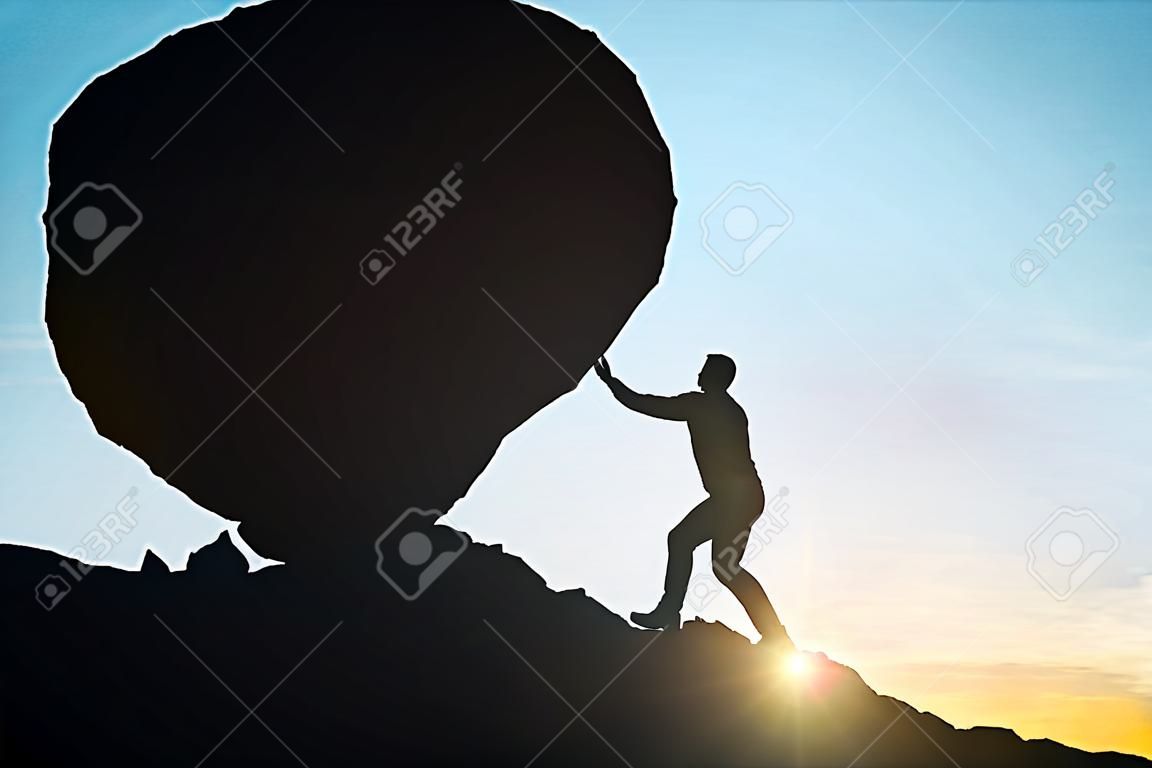 Side view of male silhouette pushing huge rock uphill. Beautiful sky background. Difficulty concept