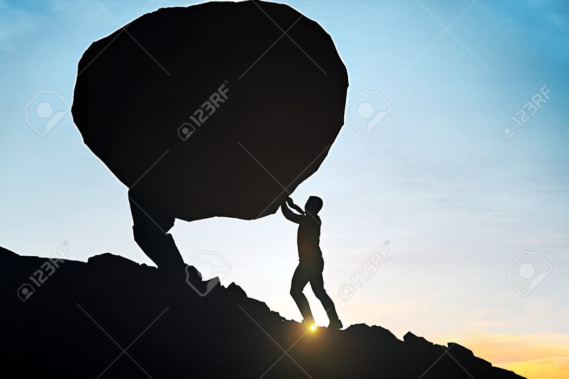 男性のサイドビューのシルエット上り坂の押すことの巨大な岩。美しい空を背景。難易度の概念