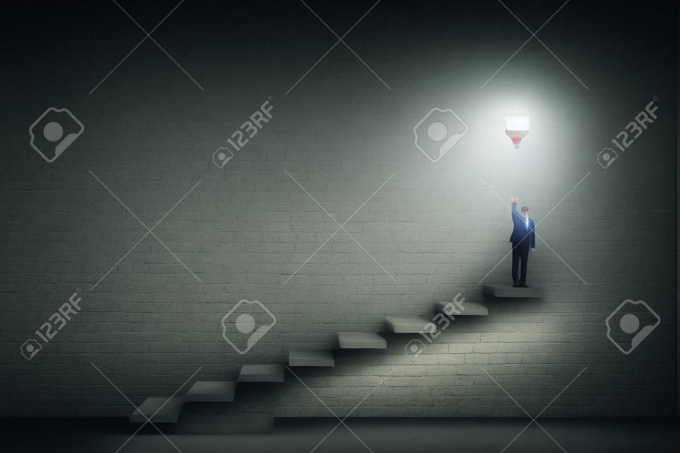 Concetto creativo e ideativo con vista frontale sull'uomo in tuta in cima alla scalinata che accende una grande lampadina su sfondo di cemento scuro nella sala vuota